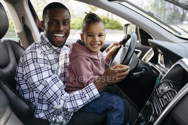 Hijo y padre jugando con el volante en el coche - foto de stock