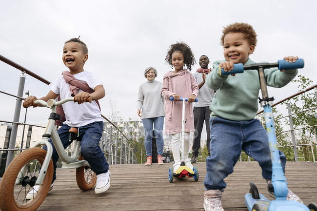 Happy children playing with push scooters and bicycle on bridge — Stock Photo