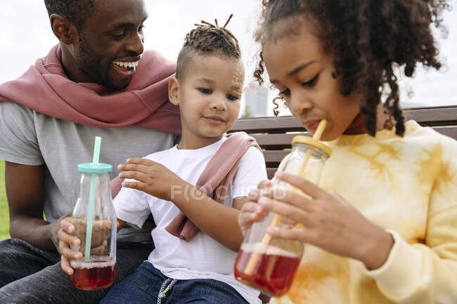Padre guardando i bambini che bevono limonata nel parco — Foto stock