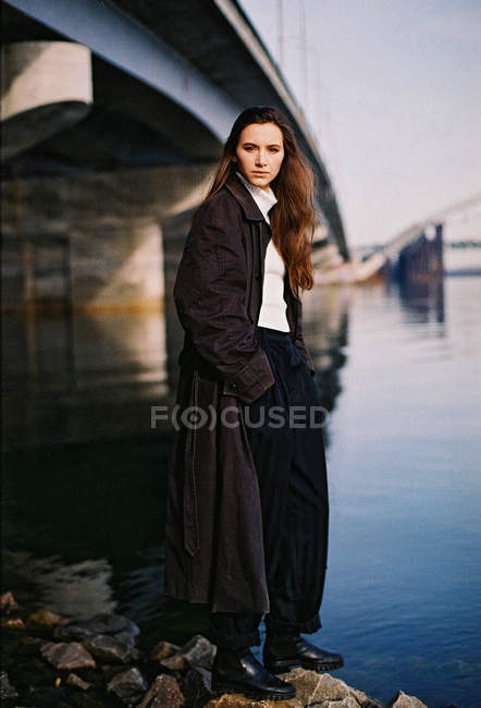 Retrato de una mujer joven con capa y de pie debajo del puente - foto de stock