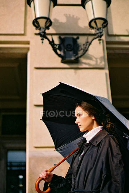 Portrait latéral de jeune femme tenant un parapluie dans la rue — Photo de stock