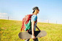 Женщина ходит с рюкзаком и скейтбордом — стоковое фото
