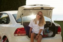 Femme assise sur le coffre de la voiture — Photo de stock