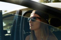 Femme en lunettes de soleil assis dans la voiture — Photo de stock