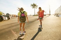Mulheres montando em skates com mochilas — Fotografia de Stock