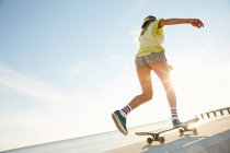 Donna che cavalca sullo skateboard sul mare — Foto stock