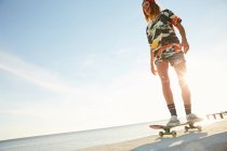 Женщина стоит со скейтбордом на берегу моря — стоковое фото