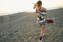 Женщина держит скейтборд на пляже — стоковое фото