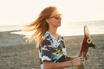 Жінка тримає скейтборд на пляжі — стокове фото