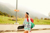 Mujer caminando con mochila y monopatín - foto de stock