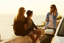Friends sitting on border at seafront — Stock Photo