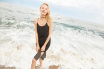 Hermosa mujer en vestido negro de pie en el mar y mirando a la cámara - foto de stock