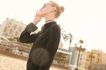 Side view of attractive woman in sunglasses standing on street at sunny day — Stock Photo
