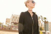 Low angle view of attractive woman in sunglasses standing on street at sunny day — Stock Photo