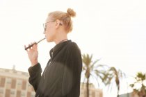 Low angle view of woman in sunglasses smoking electronic cigarette on street in barcelona — Stock Photo