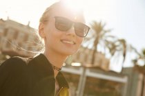 Retrato de mulher atraente sorridente em óculos de sol em pé na rua no dia ensolarado — Fotografia de Stock