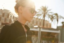 Portrait of attractive woman in sunglasses standing on street at sunny day — Stock Photo