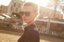 Portrait of attractive woman in sunglasses standing on street at sunny day — Stock Photo