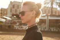 Side view of attractive girl in sunglasses standing on street at sunny day — Stock Photo