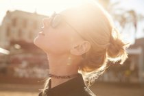 Side view of attractive woman in sunglasses standing on street at sunny day and looking up — Stock Photo