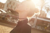 Vista laterale di donna attraente con gli occhi chiusi in piedi sulla strada nella giornata di sole — Foto stock