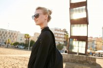 Seitenansicht einer attraktiven Frau mit Sonnenbrille und Tasche, die am öffentlichen Strand von Barcelona spazieren geht — Stockfoto