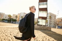 Joyeux attrayant femme dans des lunettes de soleil et sac de marche sur la plage publique à Barcelone — Photo de stock