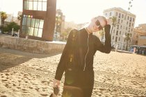Smiling attractive woman in sunglasses and bag walking on public beach in barcelona — Stock Photo