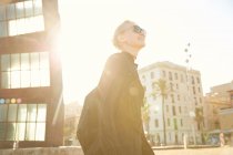 Vista de ángulo bajo de mujer atractiva en gafas de sol y bolso caminando en la playa pública en barcelona - foto de stock