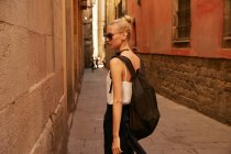 Jovem mulher em óculos de sol andando na rua estreita em barcelona — Fotografia de Stock