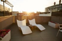 Два шезлонга и стол на террасе во время захода солнца в городе — стоковое фото