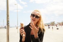 Young blonde tourist in sunglasses eating ice cream on street — Stock Photo