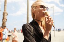 Attraktive blonde Touristin mit Sonnenbrille isst Eis auf der Straße — Stockfoto