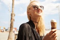 Smiling attractive blonde tourist in sunglasses eating ice cream on street — Stock Photo