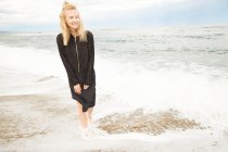 Heureuse belle femme en robe noire et sac debout dans la mer — Photo de stock