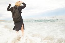 Rückansicht einer Frau in schwarzem Kleid und Tasche, die Spaß im Meer hat — Stockfoto