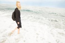 Bella donna sorridente in abito nero e borsa in piedi in mare — Foto stock