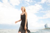 Low angle view of happy beautiful woman in black dress walking on sea beach — Stock Photo