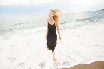 Felice bella donna in abito nero a piedi sulla spiaggia di mare — Foto stock