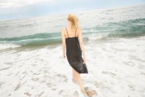 Visão traseira da mulher em vestido preto em pé no mar — Fotografia de Stock
