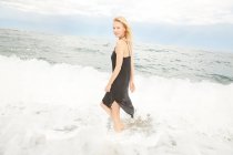 Bella donna in abito nero in piedi in mare — Foto stock