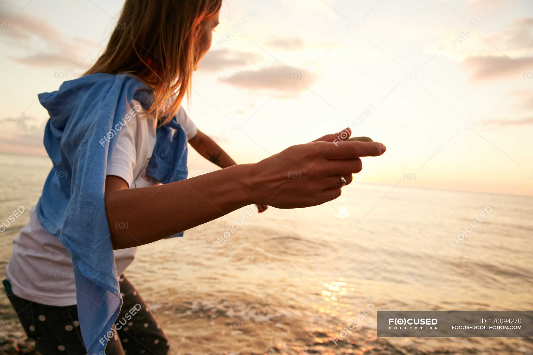 Кидаем камни в воду. Девушка с камнем в руке. Девушка кидает камень. Девушка бросающая камень. Девушка бросает камень в море.
