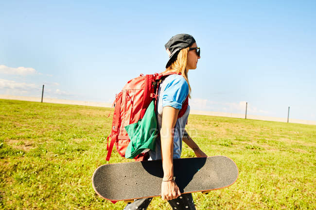 Mulher andando com mochila e skate — Fotografia de Stock
