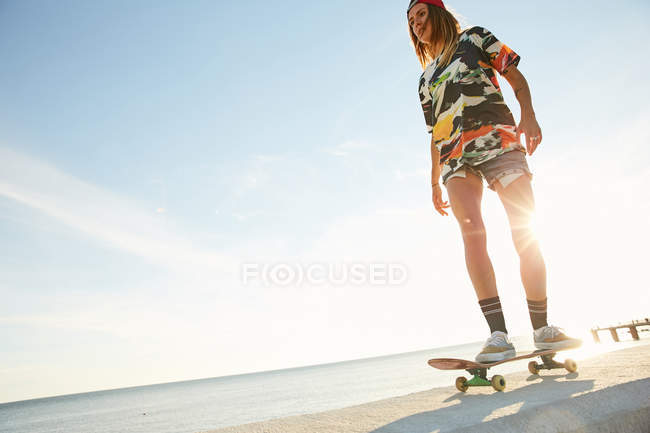 Donna in piedi con skateboard sul mare — Foto stock