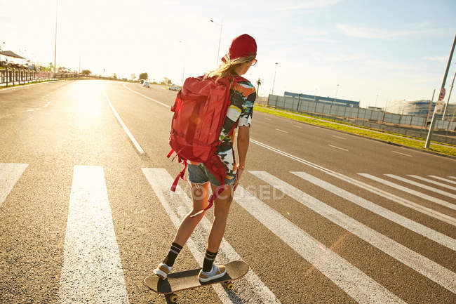 Femme chevauchant sur skateboard avec sac à dos — Photo de stock