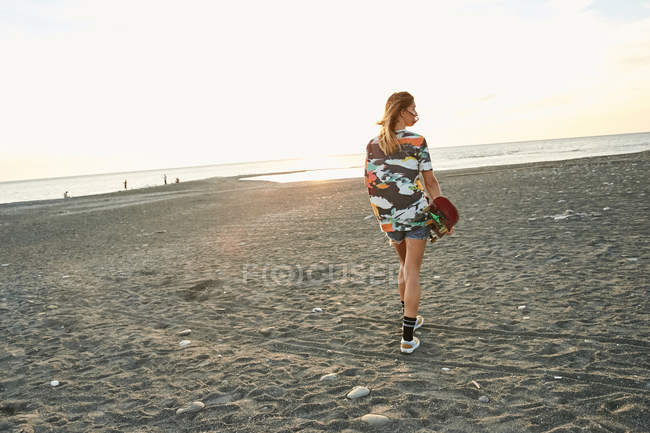 Mulher segurando skate na praia — Fotografia de Stock