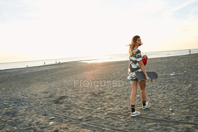 Donna che tiene lo skateboard sulla spiaggia — Foto stock