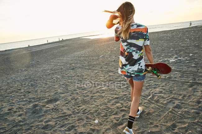 Donna che tiene lo skateboard sulla spiaggia — Foto stock