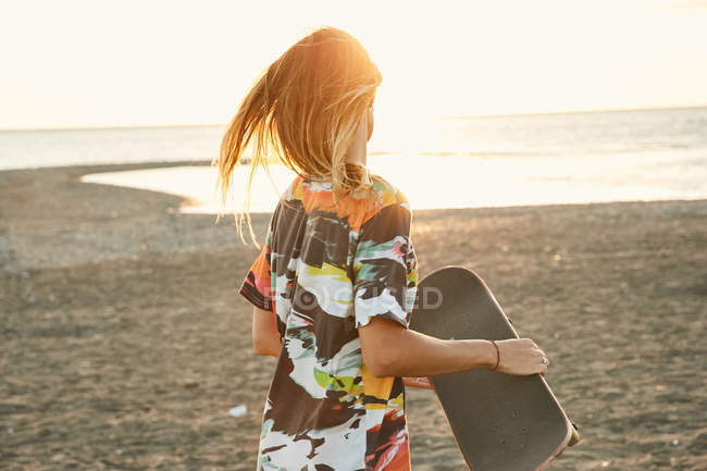 Femme tenant skateboard sur la plage — Photo de stock