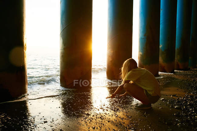 Frau sitzt neben Säulen am Strand — Stockfoto